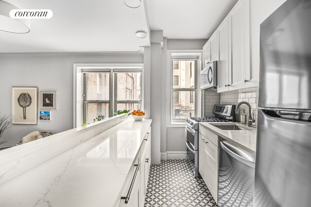 kitchen with sink, white cabinets, decorative backsplash, light stone counters, and stainless steel appliances