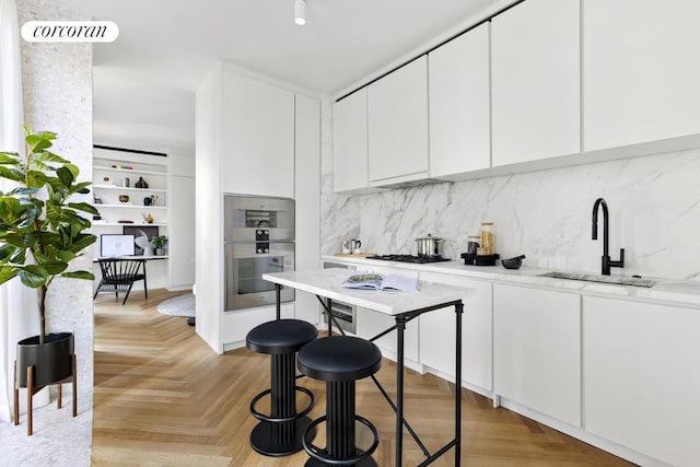 kitchen with tasteful backsplash, sink, light parquet floors, and white cabinets