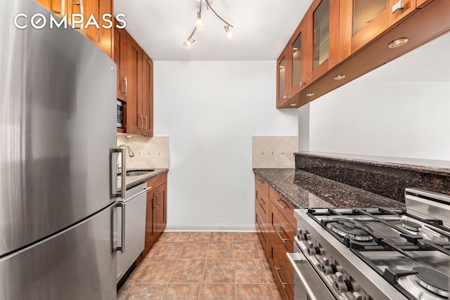 kitchen featuring tasteful backsplash, glass insert cabinets, brown cabinets, stainless steel appliances, and a sink