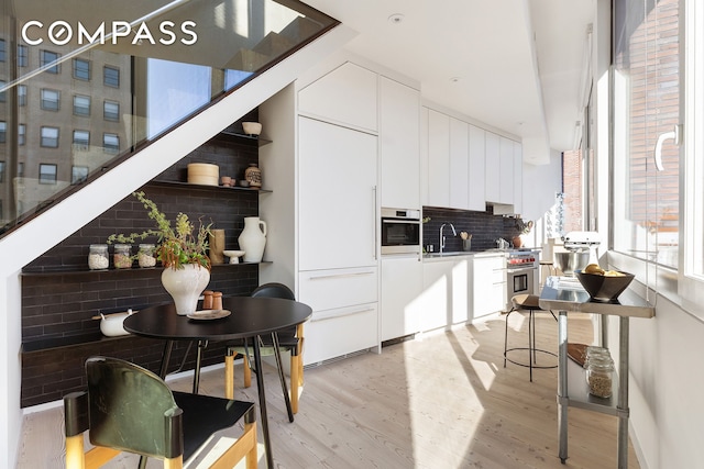 kitchen featuring tasteful backsplash, modern cabinets, oven, light wood-style floors, and a sink