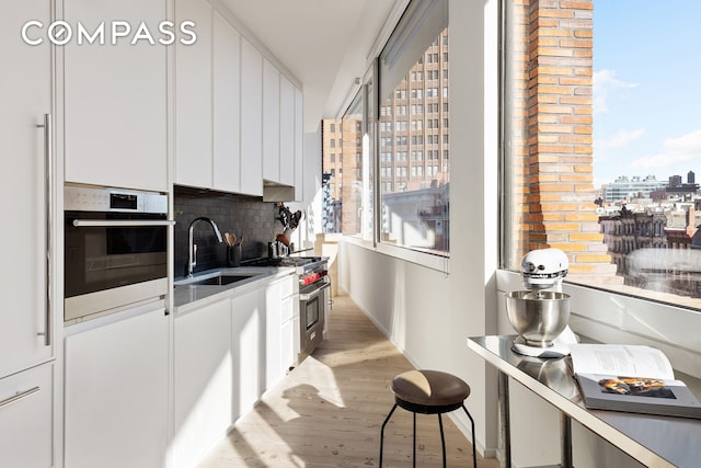 kitchen featuring oven, a sink, white cabinets, light wood-type flooring, and decorative backsplash