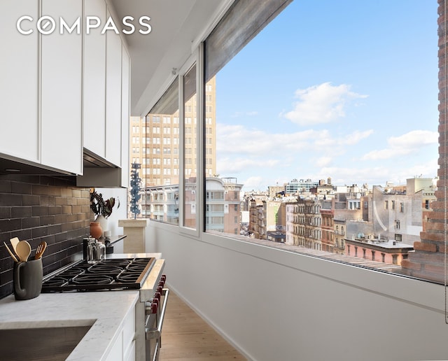 kitchen featuring a view of city, light wood-style flooring, backsplash, white cabinetry, and high end range