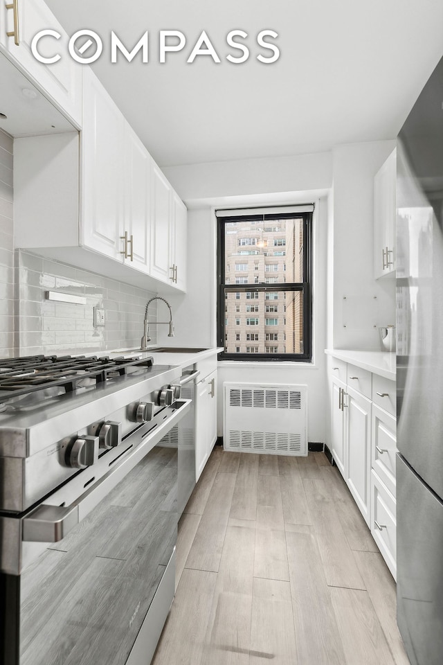 kitchen featuring a sink, backsplash, white cabinetry, radiator, and appliances with stainless steel finishes