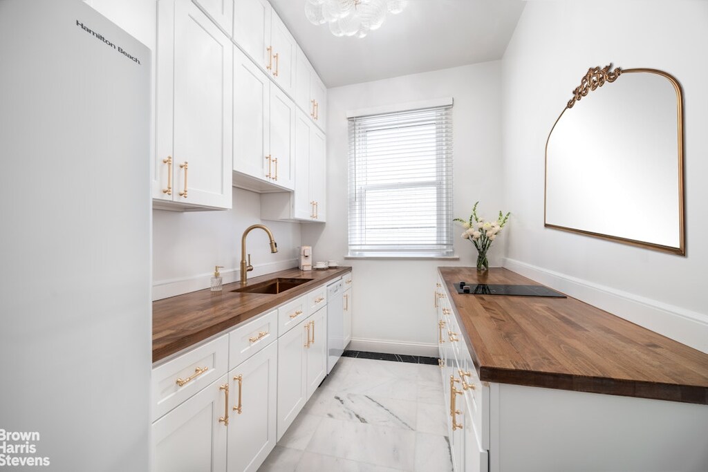 kitchen featuring freestanding refrigerator, wooden counters, black electric cooktop, white cabinets, and a sink