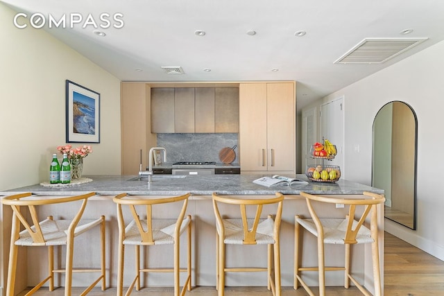 kitchen with a sink, decorative backsplash, light brown cabinetry, light wood finished floors, and modern cabinets