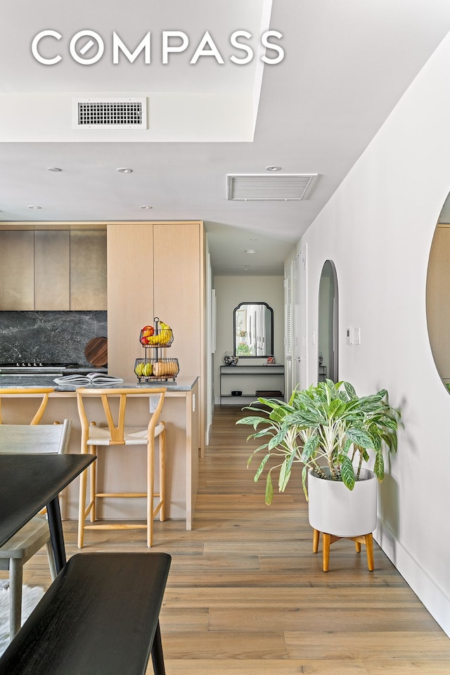 interior space with light wood-type flooring, visible vents, tasteful backsplash, and light brown cabinetry