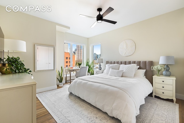 bedroom with a view of city, a ceiling fan, baseboards, and wood finished floors