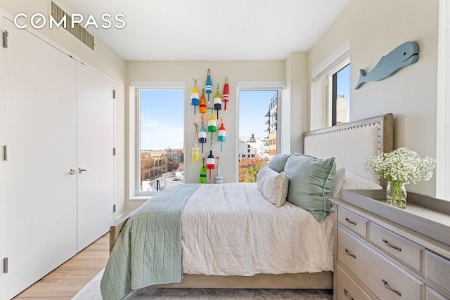 bedroom featuring light wood finished floors, visible vents, and a closet