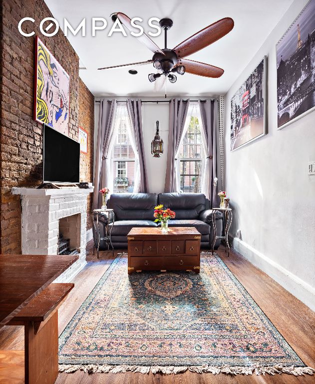 living room featuring a brick fireplace, wood-type flooring, and ceiling fan