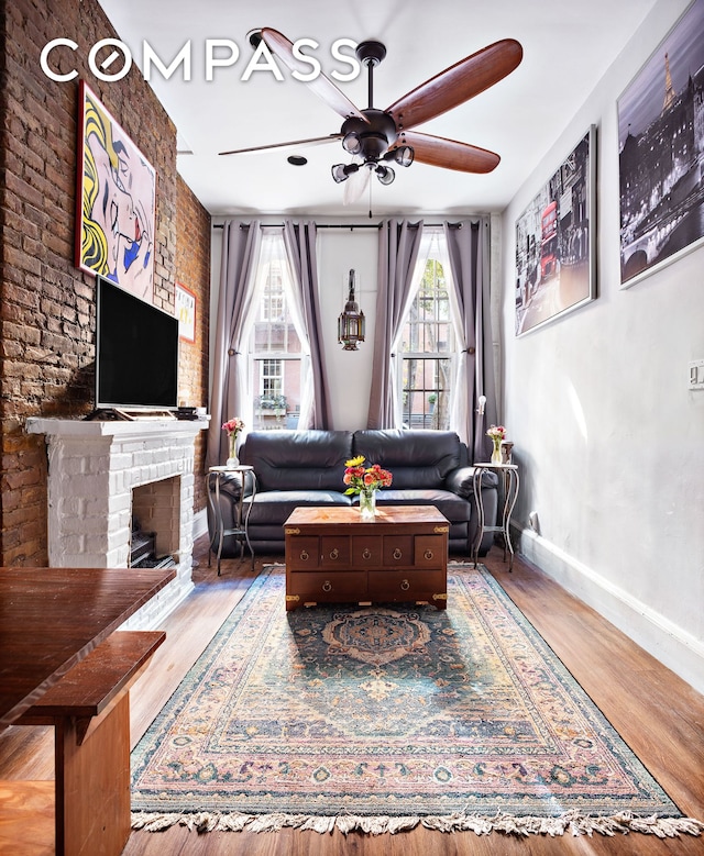 living area featuring baseboards, plenty of natural light, a brick fireplace, and wood finished floors