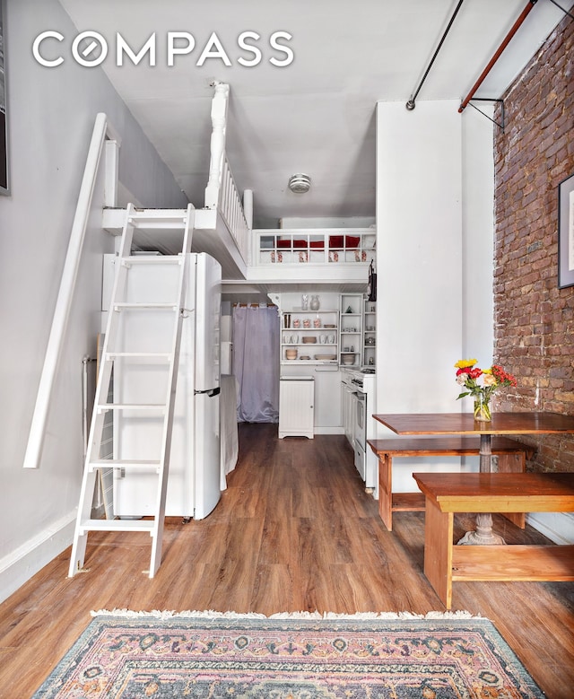 kitchen with wood finished floors, brick wall, open shelves, freestanding refrigerator, and white cabinetry