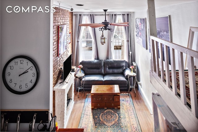 living room with ceiling fan, wood-type flooring, and a brick fireplace