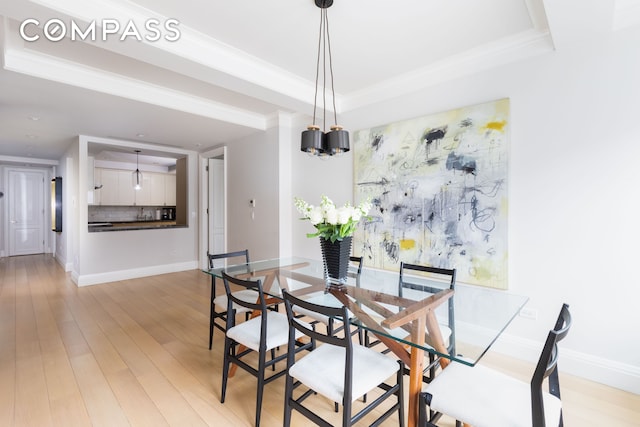 dining area featuring baseboards, a raised ceiling, light wood-style floors, and crown molding