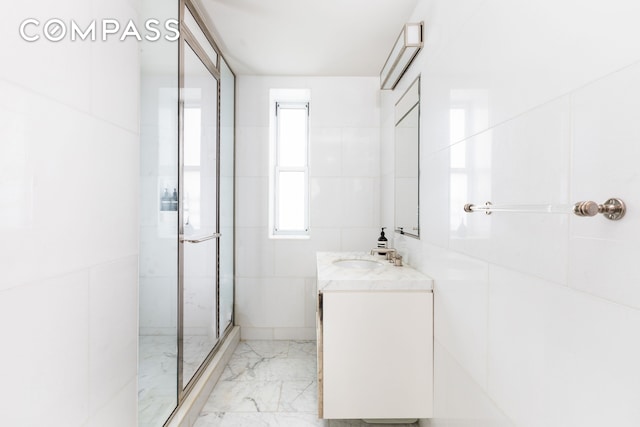 full bathroom featuring a stall shower, marble finish floor, vanity, and tile walls