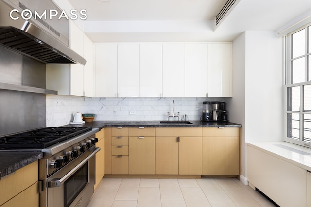 kitchen featuring backsplash, high end stove, light tile patterned floors, exhaust hood, and a sink