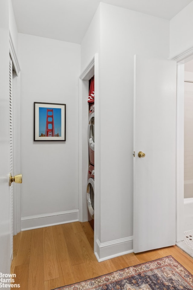 laundry room featuring laundry area, wood finished floors, stacked washer / drying machine, and baseboards