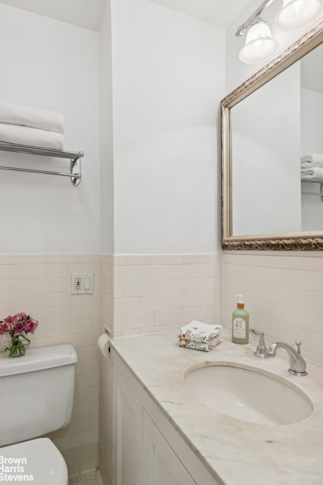 half bathroom featuring a wainscoted wall, vanity, toilet, and tile walls