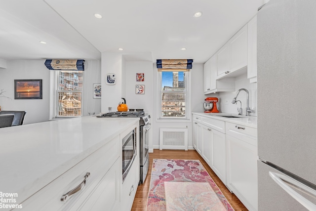 kitchen featuring light wood finished floors, light countertops, freestanding refrigerator, a sink, and gas range