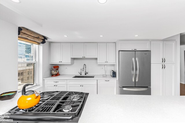 kitchen featuring a sink, light countertops, stainless steel refrigerator, and white cabinetry