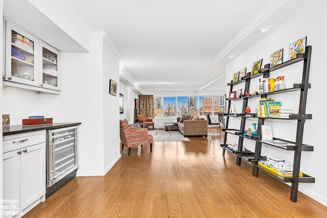 hall featuring beverage cooler, light wood-style floors, baseboards, and crown molding