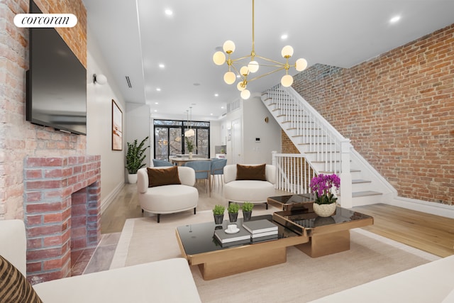 living room featuring a fireplace, brick wall, an inviting chandelier, and light wood-type flooring