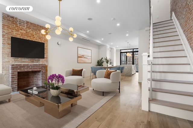 living room with light wood-type flooring, a brick fireplace, and an inviting chandelier