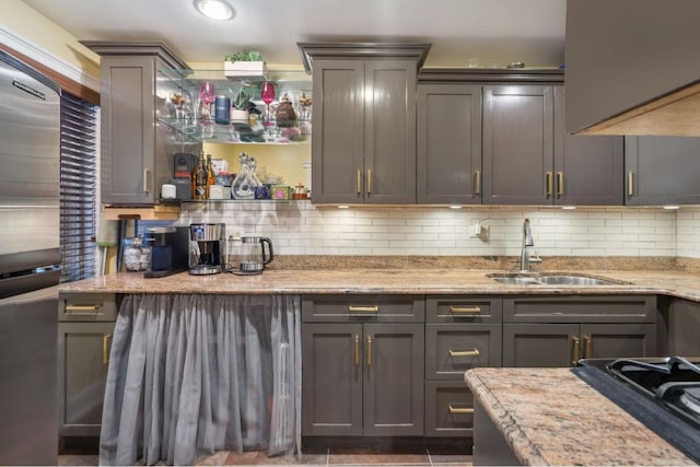 kitchen with tasteful backsplash, light stone countertops, sink, and black gas cooktop