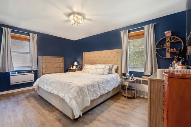 bedroom featuring hardwood / wood-style flooring, radiator heating unit, and a wall unit AC