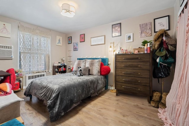 bedroom featuring a wall mounted air conditioner, radiator heating unit, and light hardwood / wood-style floors