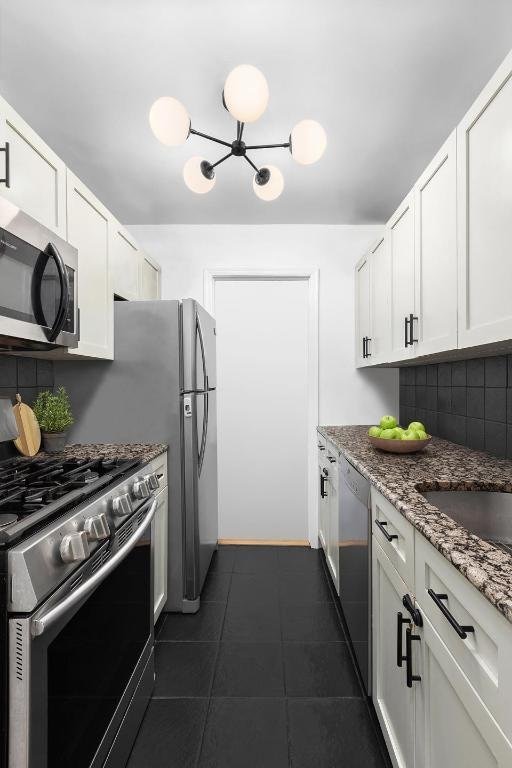 kitchen with stainless steel appliances, white cabinetry, stone counters, and dark tile patterned flooring