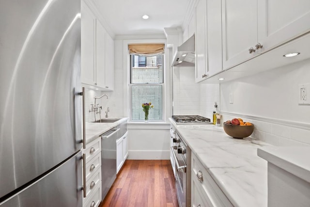 kitchen with wall chimney exhaust hood, sink, light stone counters, appliances with stainless steel finishes, and white cabinets