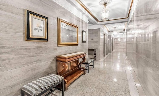 hall with granite finish floor, ornamental molding, and a chandelier