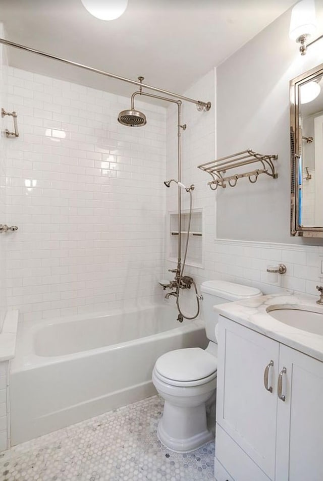 bathroom with a wainscoted wall, tile walls, toilet, washtub / shower combination, and vanity