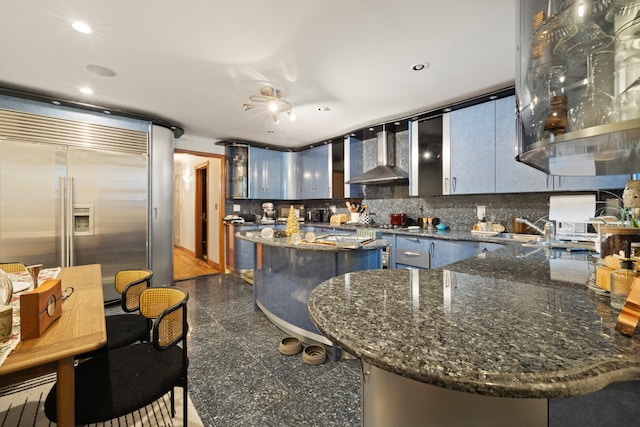 kitchen with decorative backsplash, wall chimney exhaust hood, a kitchen island, built in refrigerator, and a sink