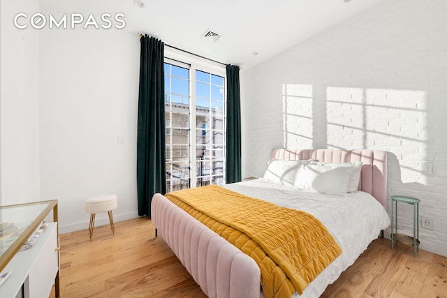 bedroom featuring light wood-type flooring, lofted ceiling, visible vents, and brick wall