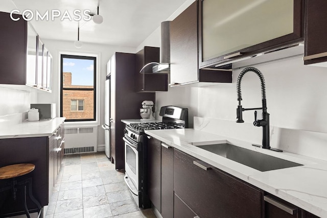 kitchen with sink, radiator heating unit, fridge, light stone counters, and stainless steel gas range oven