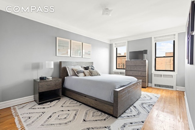 bedroom with crown molding, radiator heating unit, light wood-type flooring, and baseboards