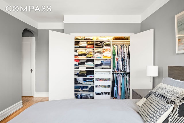 bedroom featuring wood finished floors, baseboards, arched walkways, and a closet