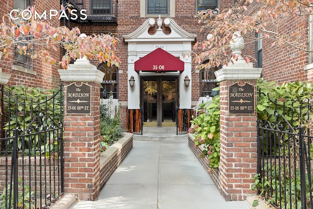 view of exterior entry featuring brick siding, french doors, and fence