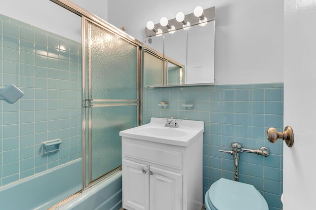 full bathroom featuring tile walls, vanity, toilet, and combined bath / shower with glass door