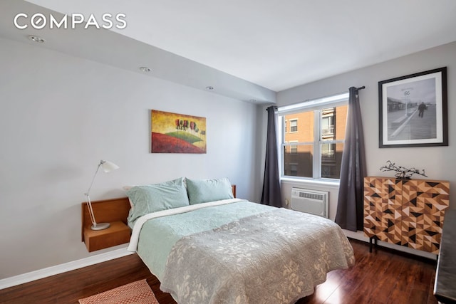 bedroom featuring a wall unit AC, wood finished floors, and baseboards