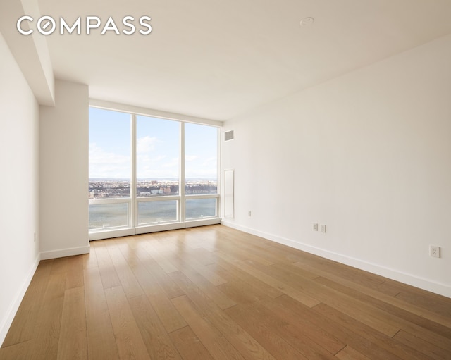 unfurnished room featuring baseboards, visible vents, a wall of windows, and wood finished floors