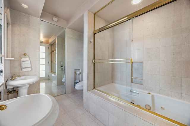 bathroom with tile walls, toilet, a combined bath / shower with jetted tub, tile patterned flooring, and a sink