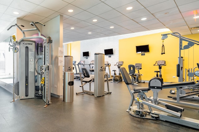 exercise room featuring a paneled ceiling, brick wall, and recessed lighting