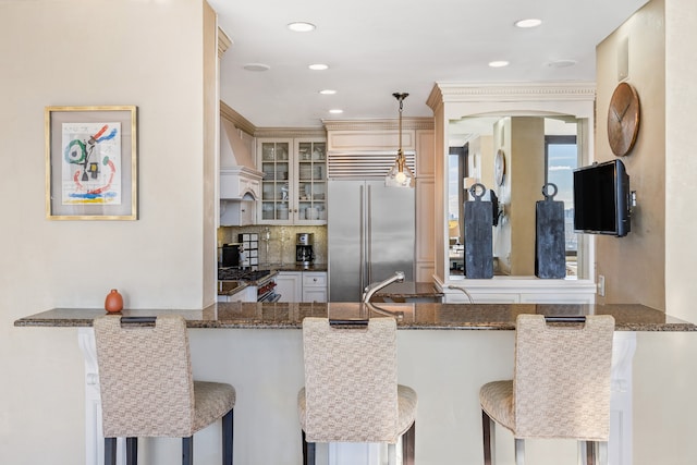 kitchen with hanging light fixtures, decorative backsplash, appliances with stainless steel finishes, glass insert cabinets, and a peninsula