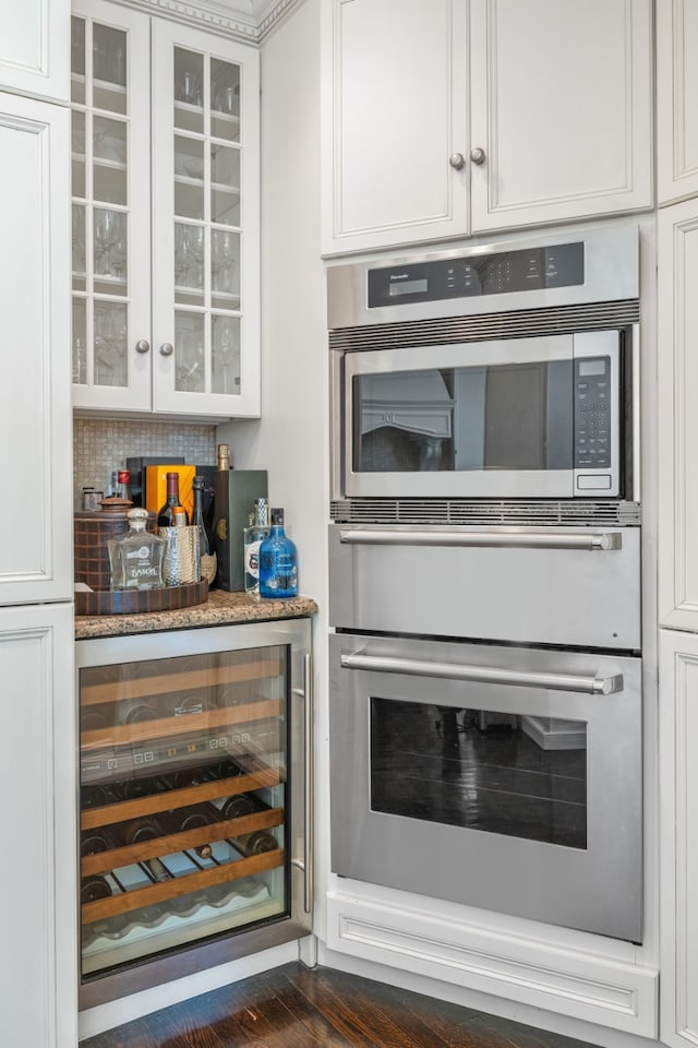 bar featuring double oven, wine cooler, decorative backsplash, a bar, and dark wood finished floors