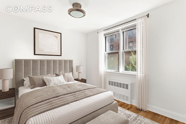 bedroom with radiator heating unit, baseboards, and wood finished floors