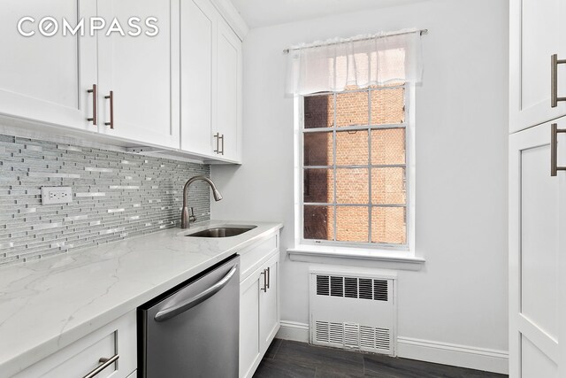 bar featuring sink, radiator heating unit, light stone countertops, white cabinets, and stainless steel dishwasher