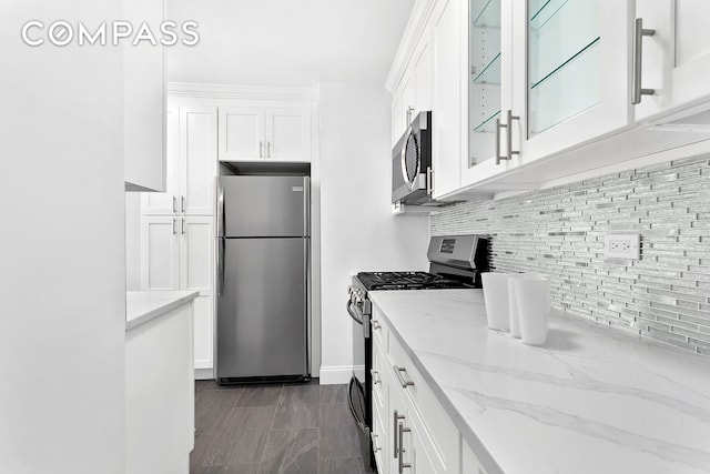 kitchen featuring light stone counters, tasteful backsplash, stainless steel appliances, white cabinets, and glass insert cabinets