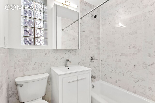 full bathroom with tiled shower / bath, vanity, toilet, and tile walls